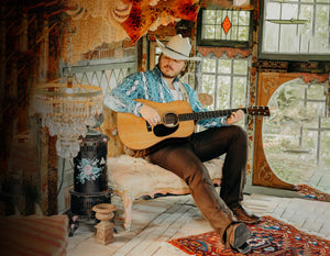 Caleb Lee Hutchinson in a room of windows playing his guitar.